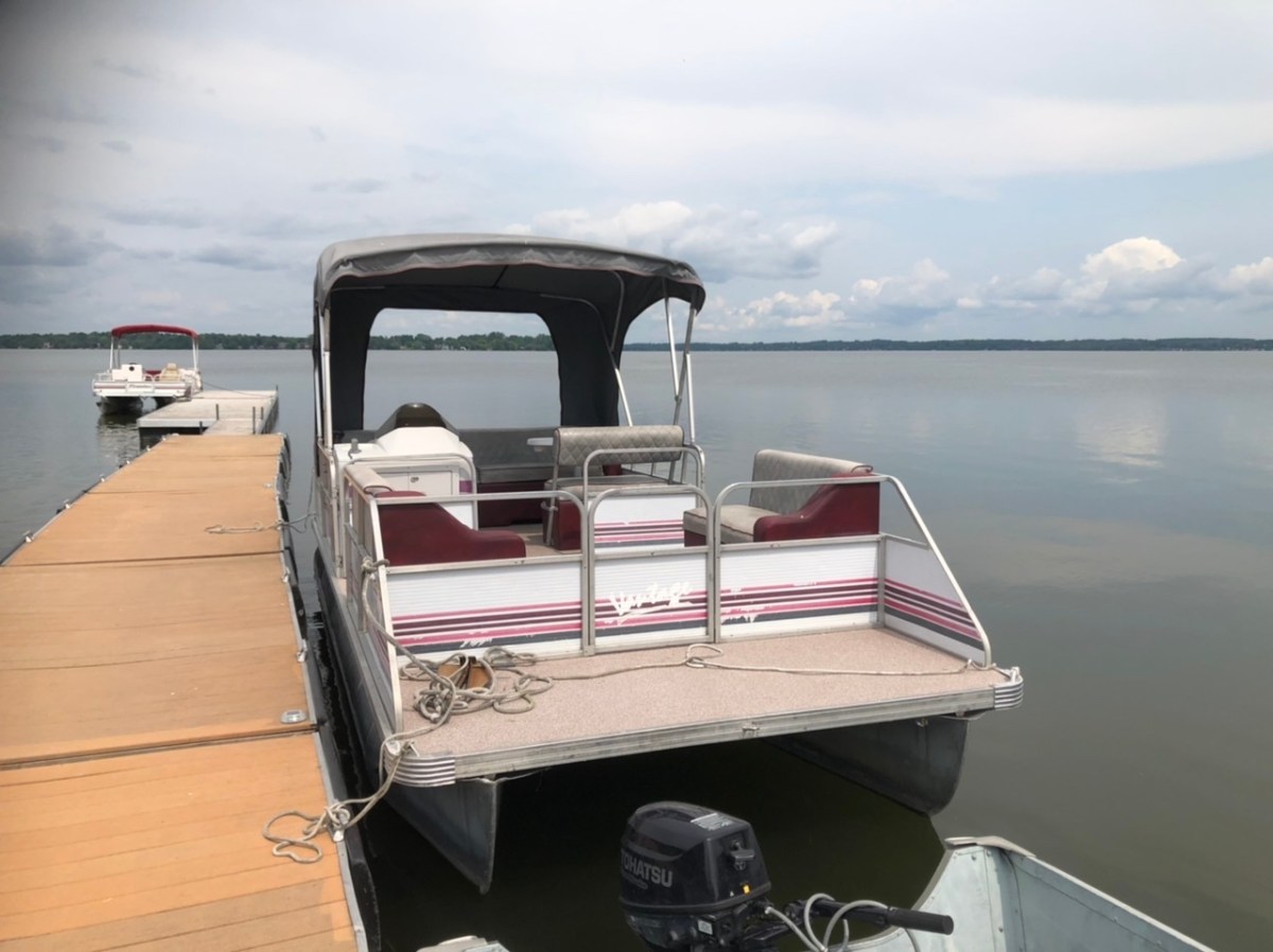 Pontoon boat docked on a calm lake under a cloudy sky.