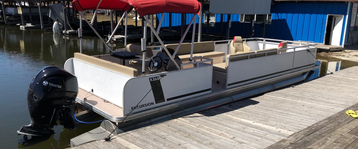 Pontoon boat with red canopy docked beside wooden pier on a sunny day.