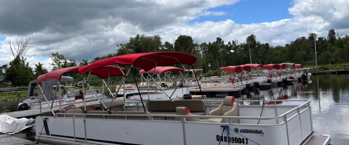 Row of pontoon boats with red canopies docked at a marina under a cloudy sky.