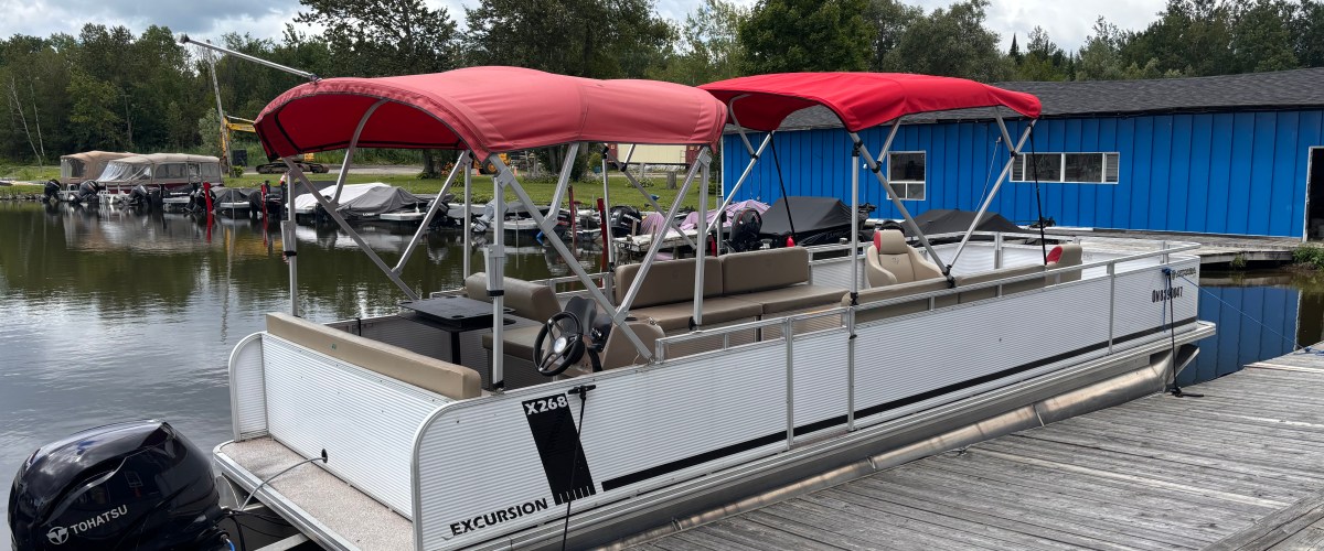 Pontoon boat with red canopies docked by a wooden pier.