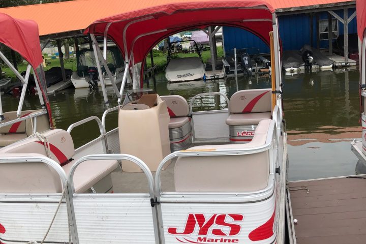 Pontoon boat with red canopy and seats docked by a pier.