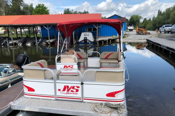 Small red and white boat docked by a waterfront with trees and buildings.