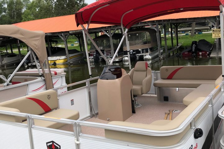 Pontoon boat with red canopy, beige seats, and trees in the background.