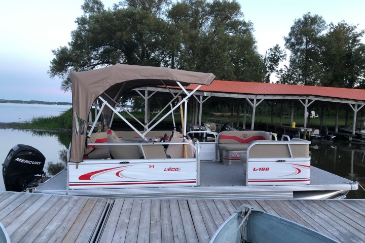 Pontoon boat docked on a wooden pier with a canopy and red-striped seats.