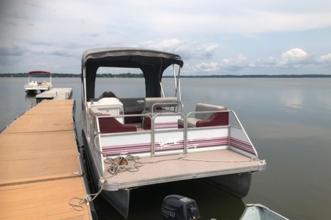 Pontoon boat docked on a calm lake with overcast sky.